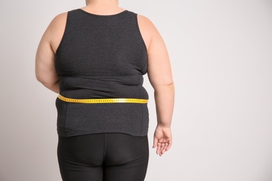 Photo of Overweight woman with measuring tape on light background