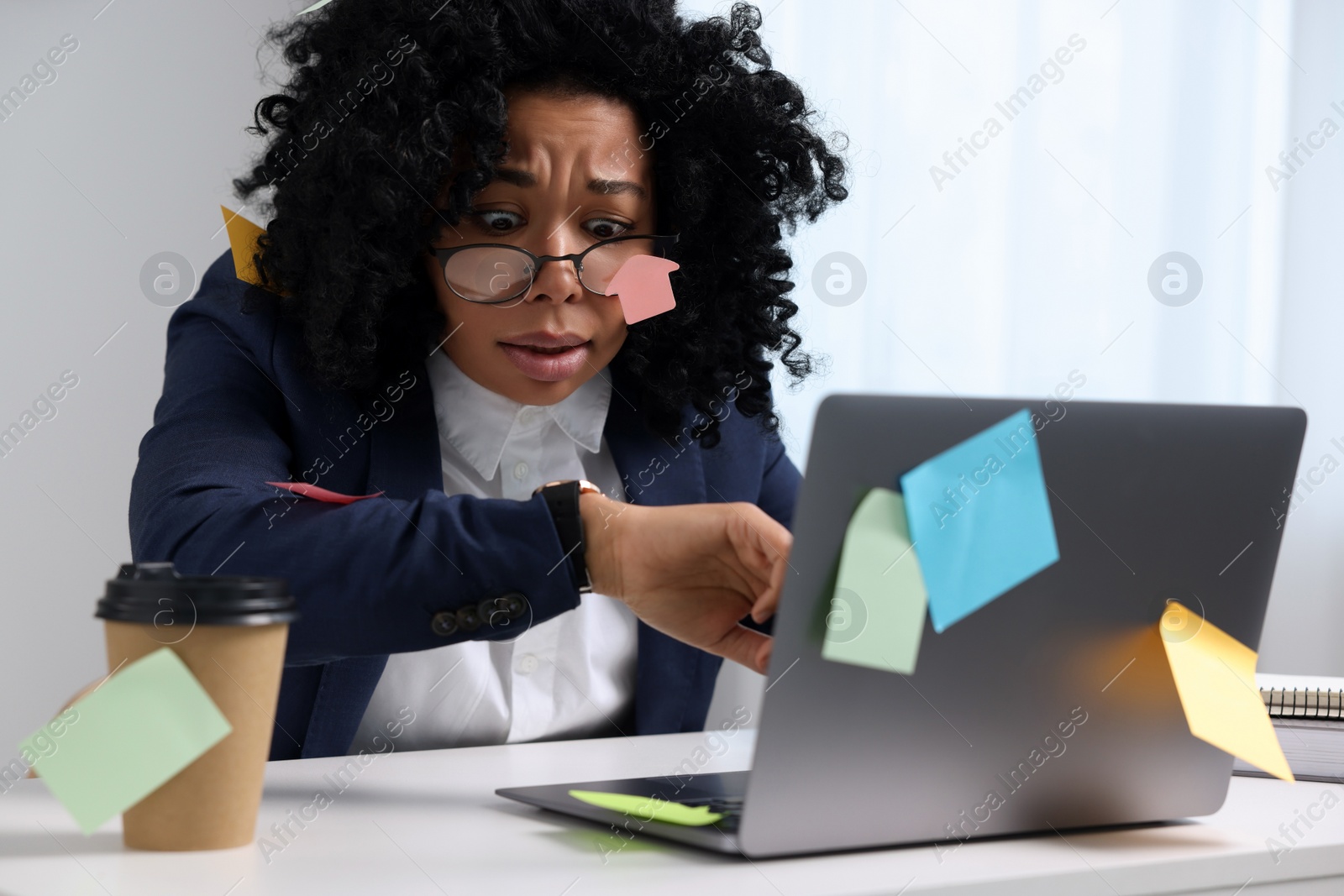 Photo of Deadline concept. Stressed woman checking time near laptop in office. Many sticky notes everywhere as reminders