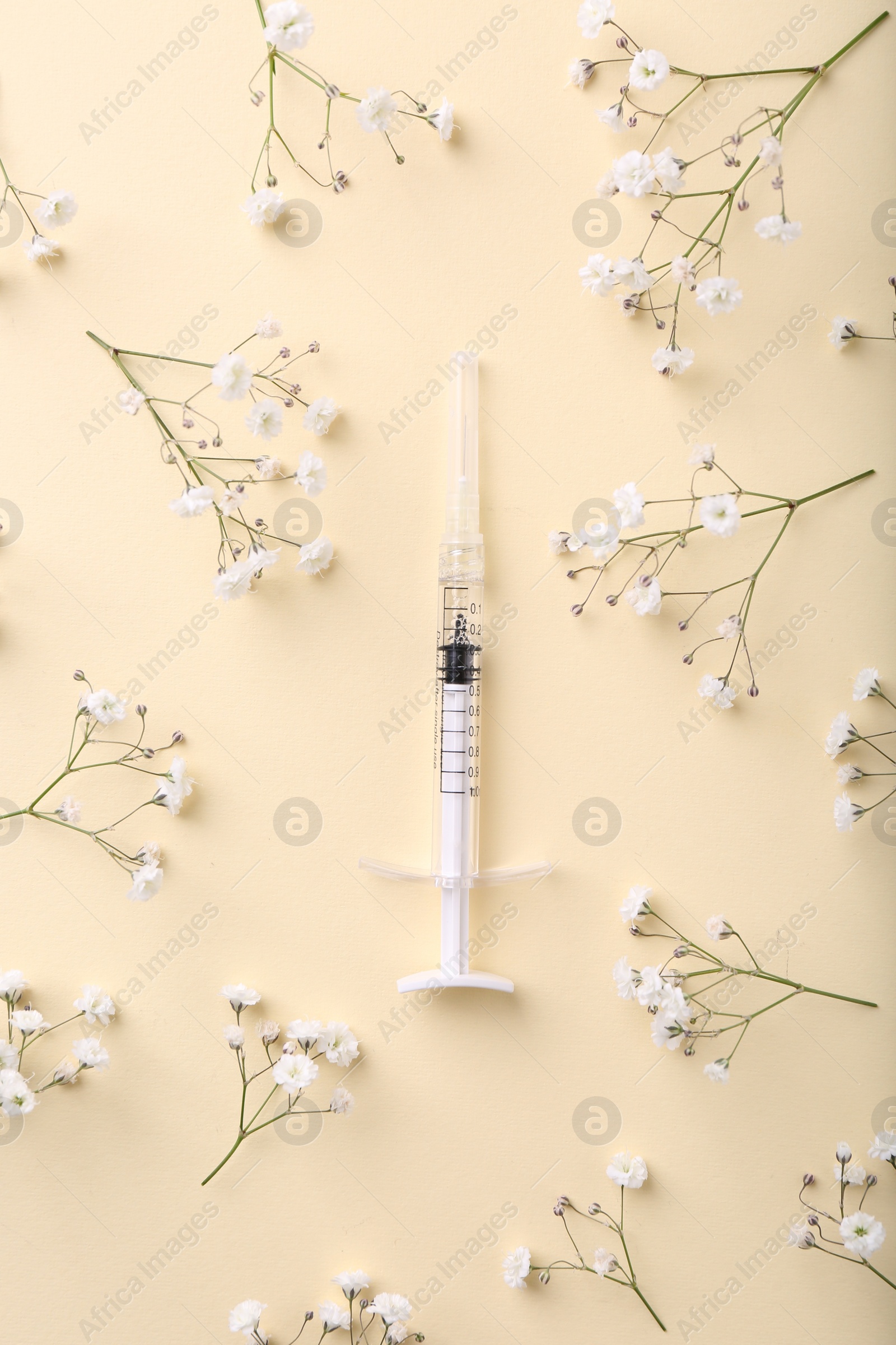 Photo of Cosmetology. Medical syringe and gypsophila flowers on yellow background, flat lay