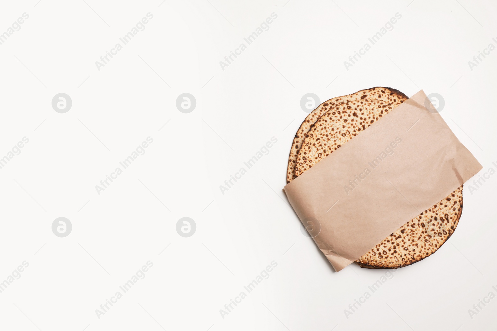 Photo of Tasty matzos wrapped with paper on white background, top view. Passover (Pesach) celebration