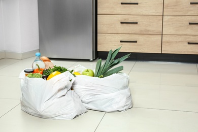 Photo of Plastic bags with vegetables and other products on floor in kitchen. Space for text