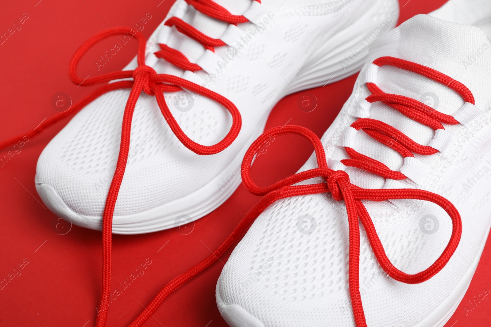 Photo of Stylish sneakers with shoe laces on red background, closeup