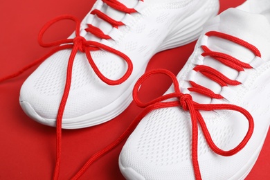 Photo of Stylish sneakers with shoe laces on red background, closeup