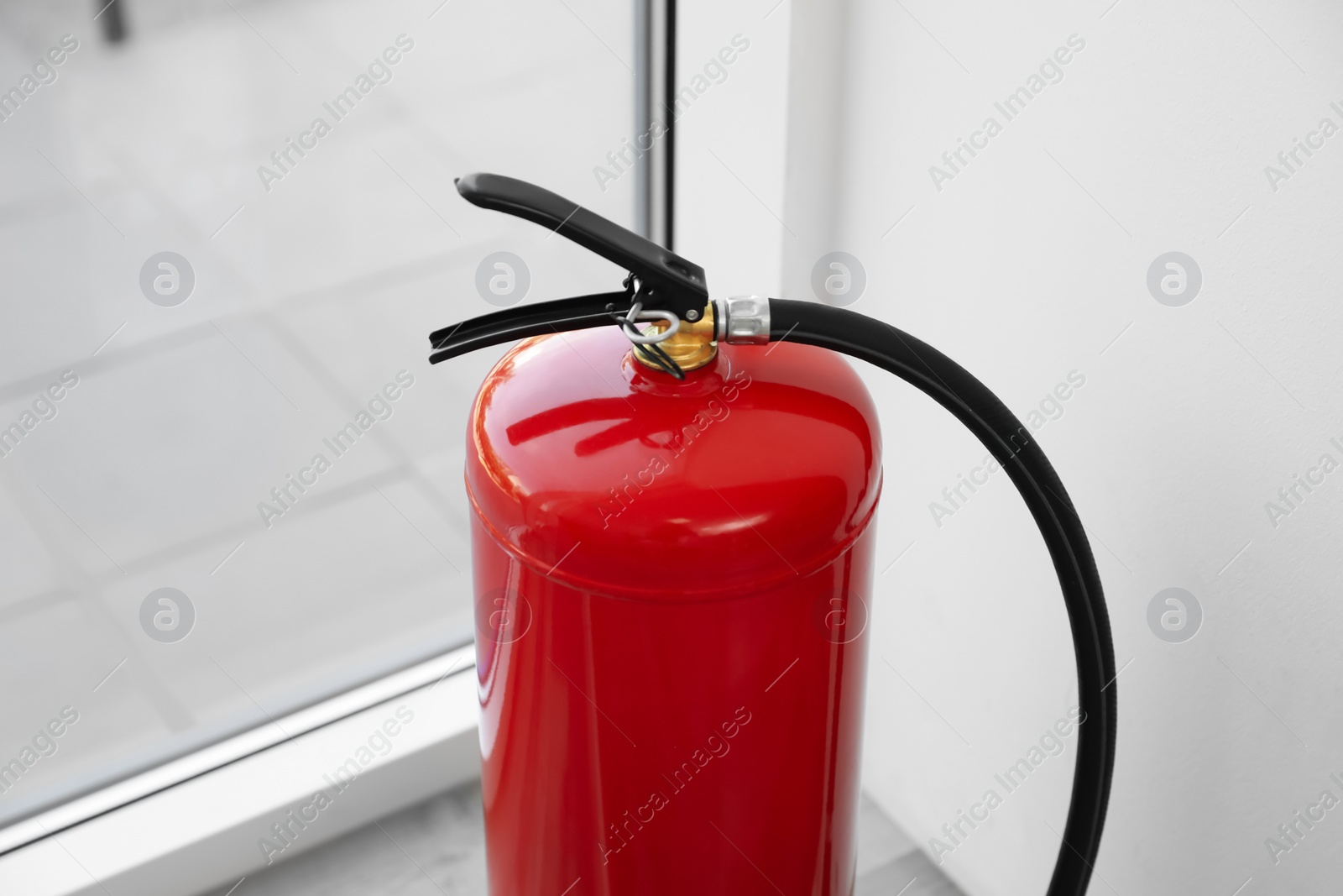 Photo of Modern fire extinguisher near window indoors, closeup