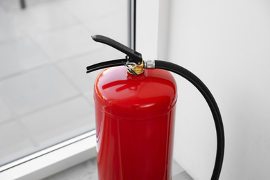 Photo of Modern fire extinguisher near window indoors, closeup