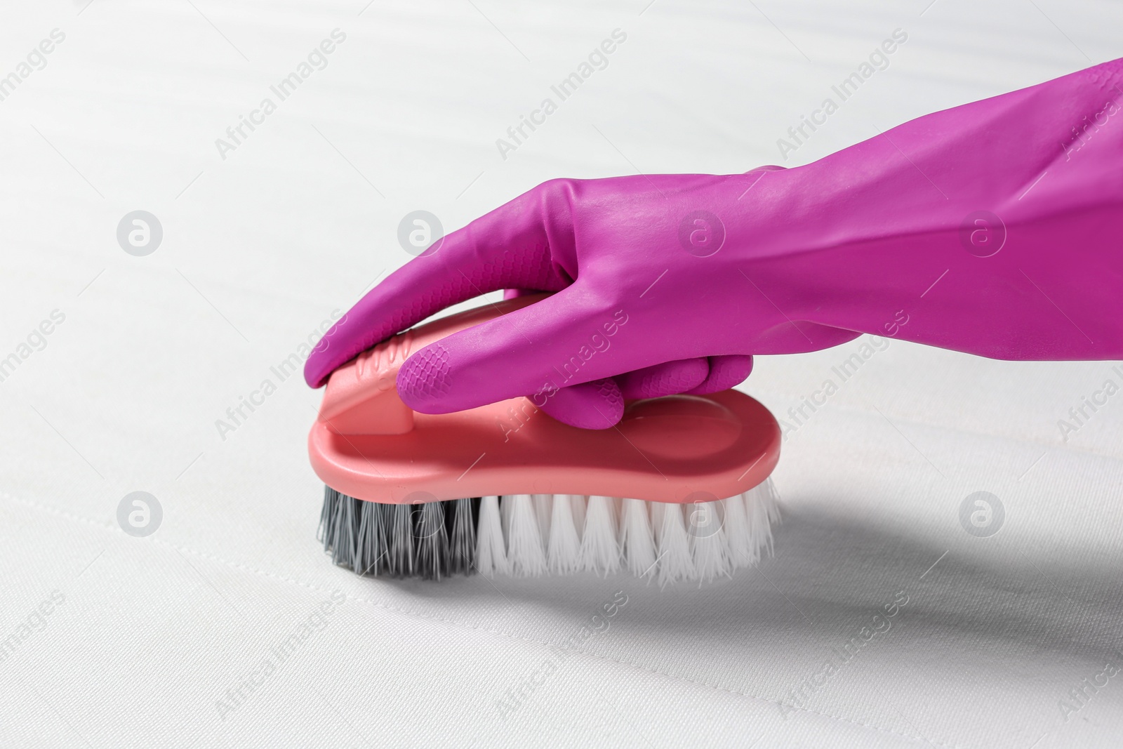 Photo of Woman in purple gloves cleaning white mattress with brush, closeup