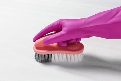 Woman in purple gloves cleaning white mattress with brush, closeup