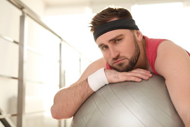 Photo of Lazy young man with exercise ball indoors