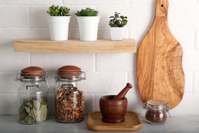 Wooden dishware and different products on grey table near white brick wall in kitchen