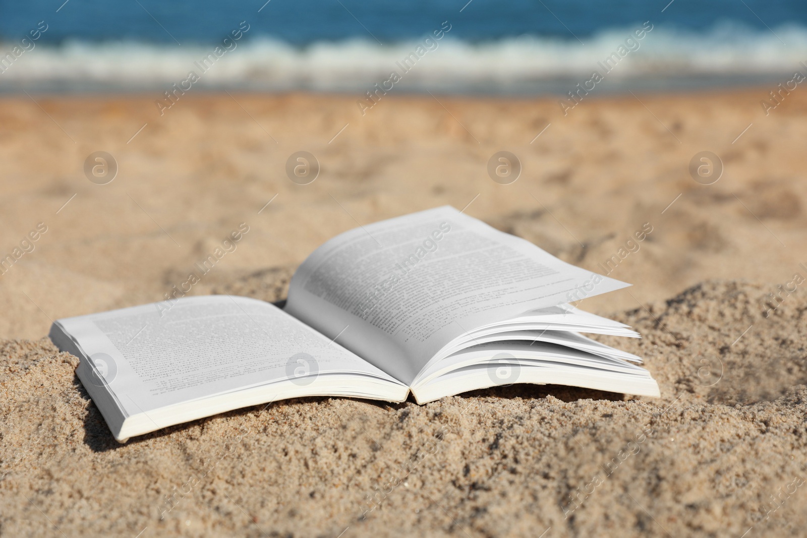 Photo of Open book on sandy beach near sea