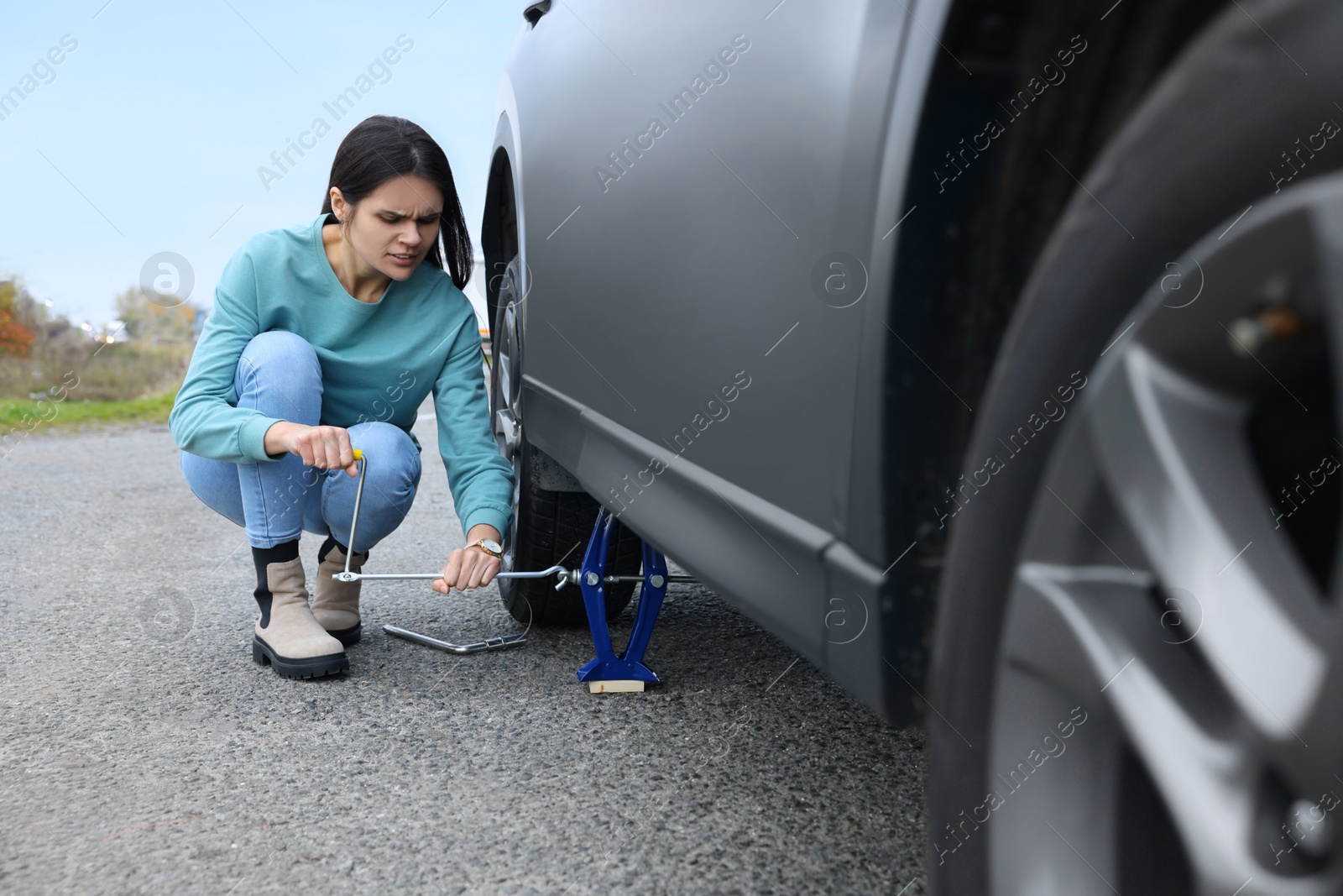 Photo of Young woman changing tire of car on roadside