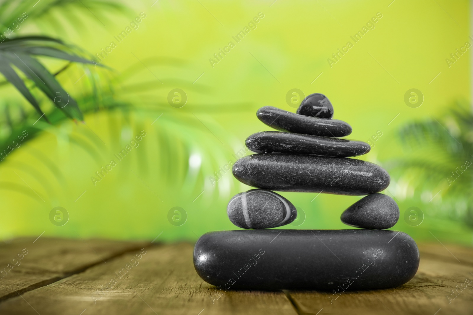 Photo of Table with stack of stones and blurred green leaves on background, space for text. Zen concept