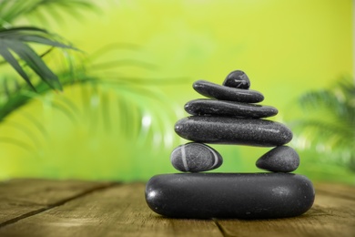 Photo of Table with stack of stones and blurred green leaves on background, space for text. Zen concept