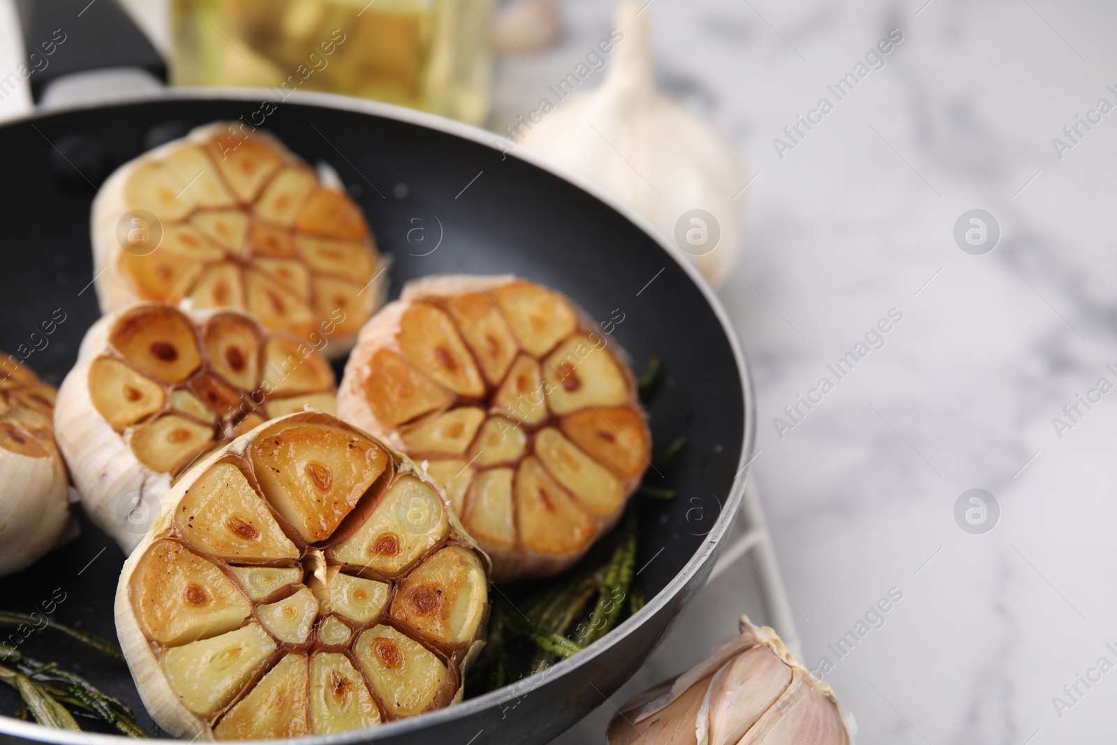 Photo of Frying pan with fried garlic and rosemary on light table, closeup. Space for text