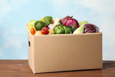 Photo of Fresh vegetables in cardboard box on wooden table