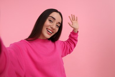 Photo of Smiling young woman taking selfie on pink background, space for text