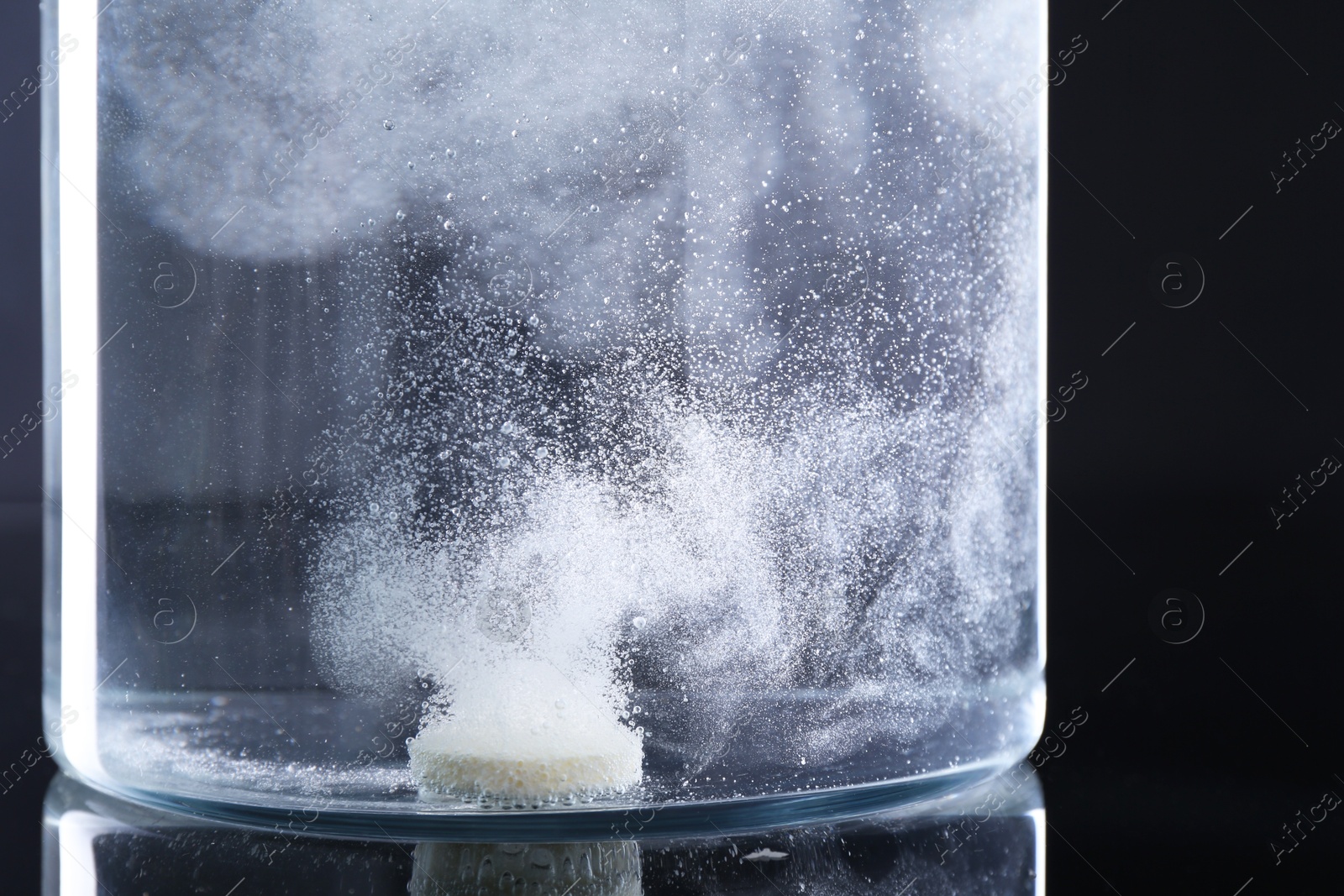 Photo of Effervescent pill dissolving in glass of water on black background, closeup