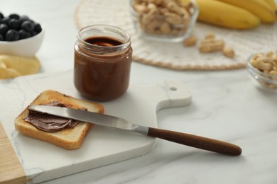 Photo of Toast with tasty nut butter, knife and jar on white marble table