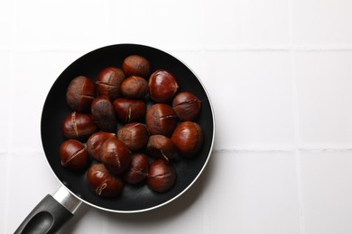 Fresh edible sweet chestnuts in frying pan on white tiled table, top view. Space for text