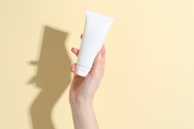 Woman holding tube of cream on yellow background, closeup