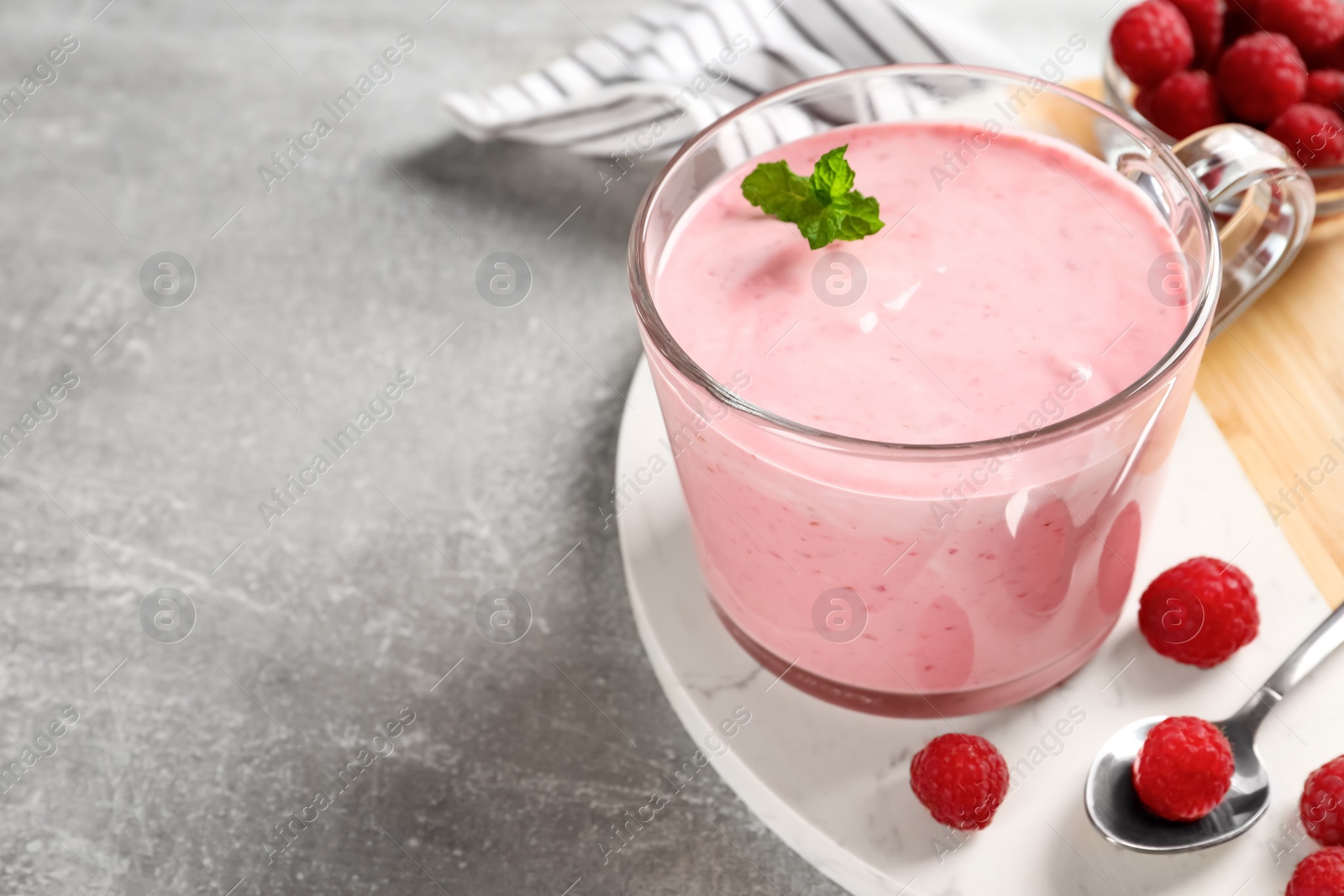 Photo of Glass of delicious yogurt with mint and raspberries on grey table, closeup. Space for text