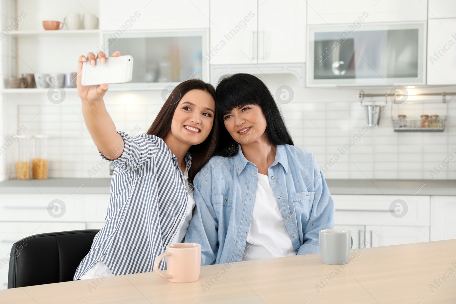 Photo of Young woman and her mature mother taking selfie at table indoors