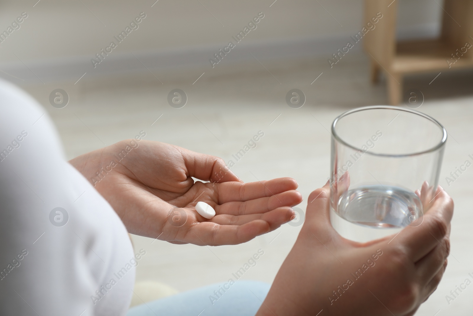 Photo of Woman with glass of water and pill on blurred background, closeup