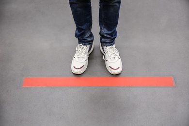 Photo of Person standing behind taped floor marking indoors for social distance, closeup. Preventive measure during coronavirus pandemic