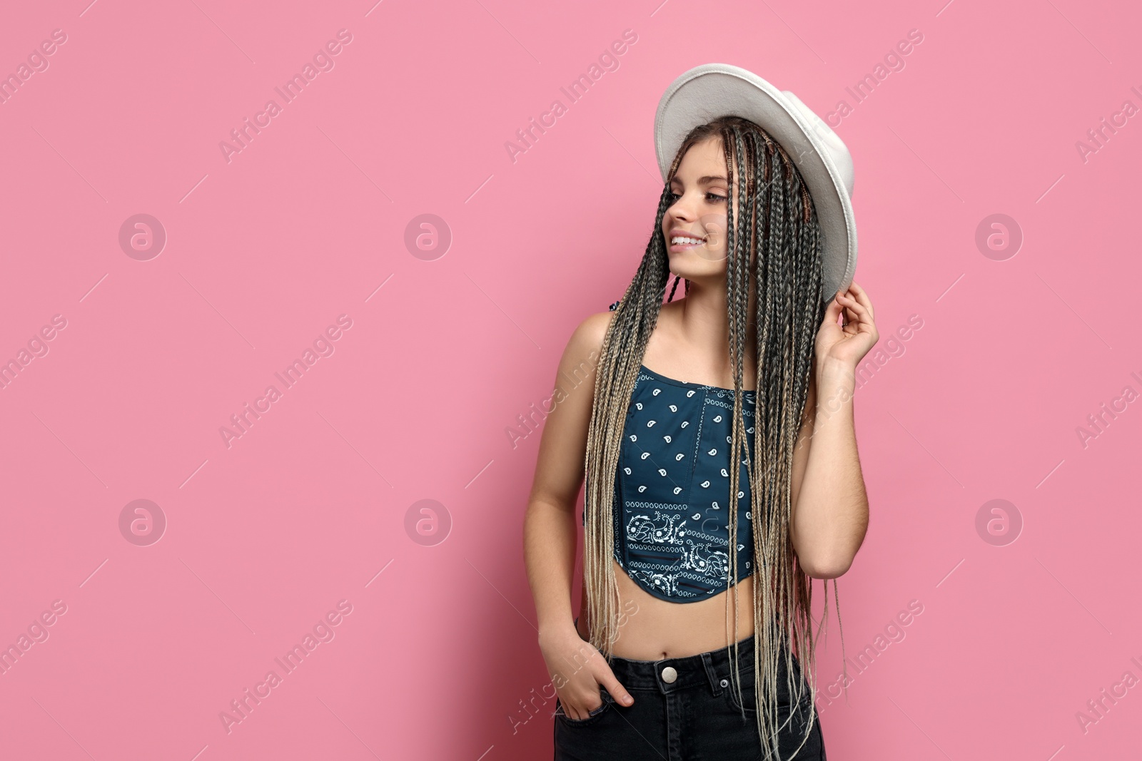 Photo of Beautiful woman with long african braids and hat on pink background, space for text