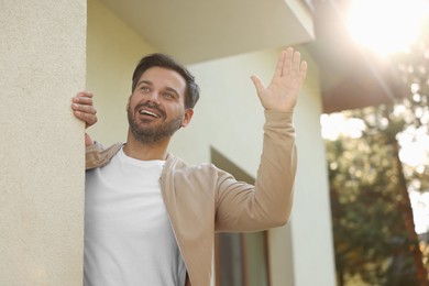 Photo of Neighbor greeting. Happy man waving near house outdoors, low angle view