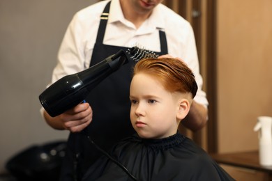 Photo of Professional hairdresser drying boy's hair in beauty salon, closeup