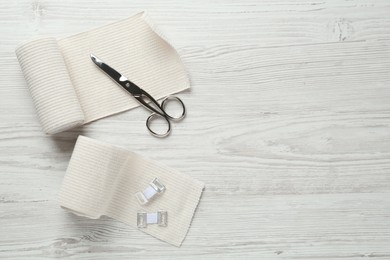 Photo of Medical bandage rolls and scissors on white wooden table, flat lay. Space for text