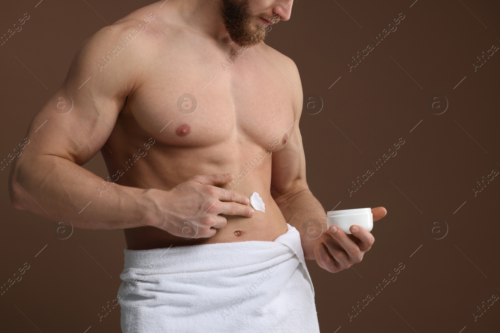 Photo of Man applying moisturizing cream onto his body on brown background, closeup