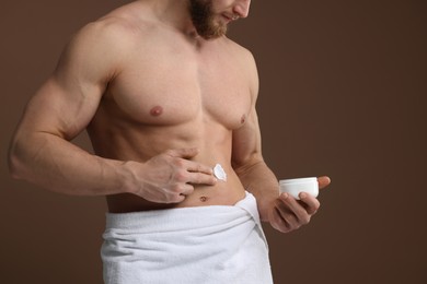 Photo of Man applying moisturizing cream onto his body on brown background, closeup