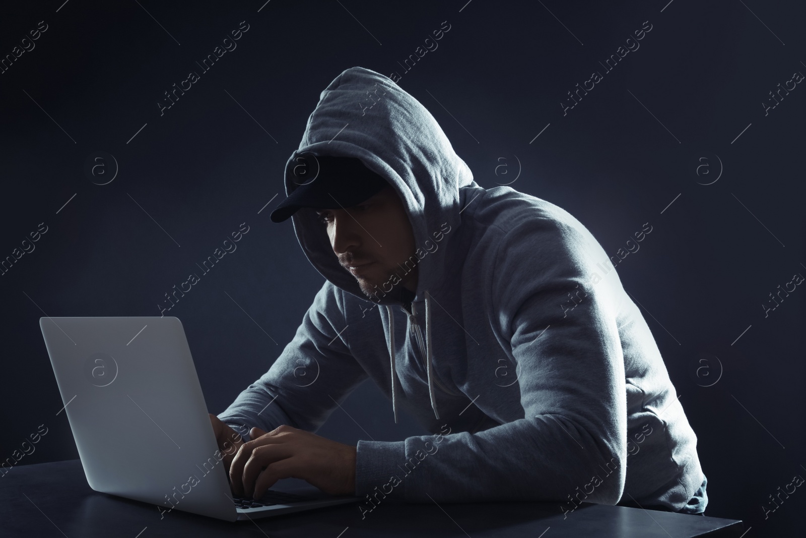 Photo of Man using laptop at table on dark background. Criminal activity