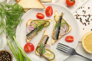 Photo of Delicious sandwiches with sprats, pickled cucumber, onion and dill served on white wooden table, flat lay