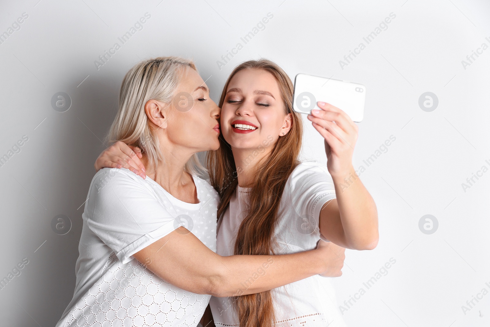 Photo of Happy mother and daughter taking selfie on white background