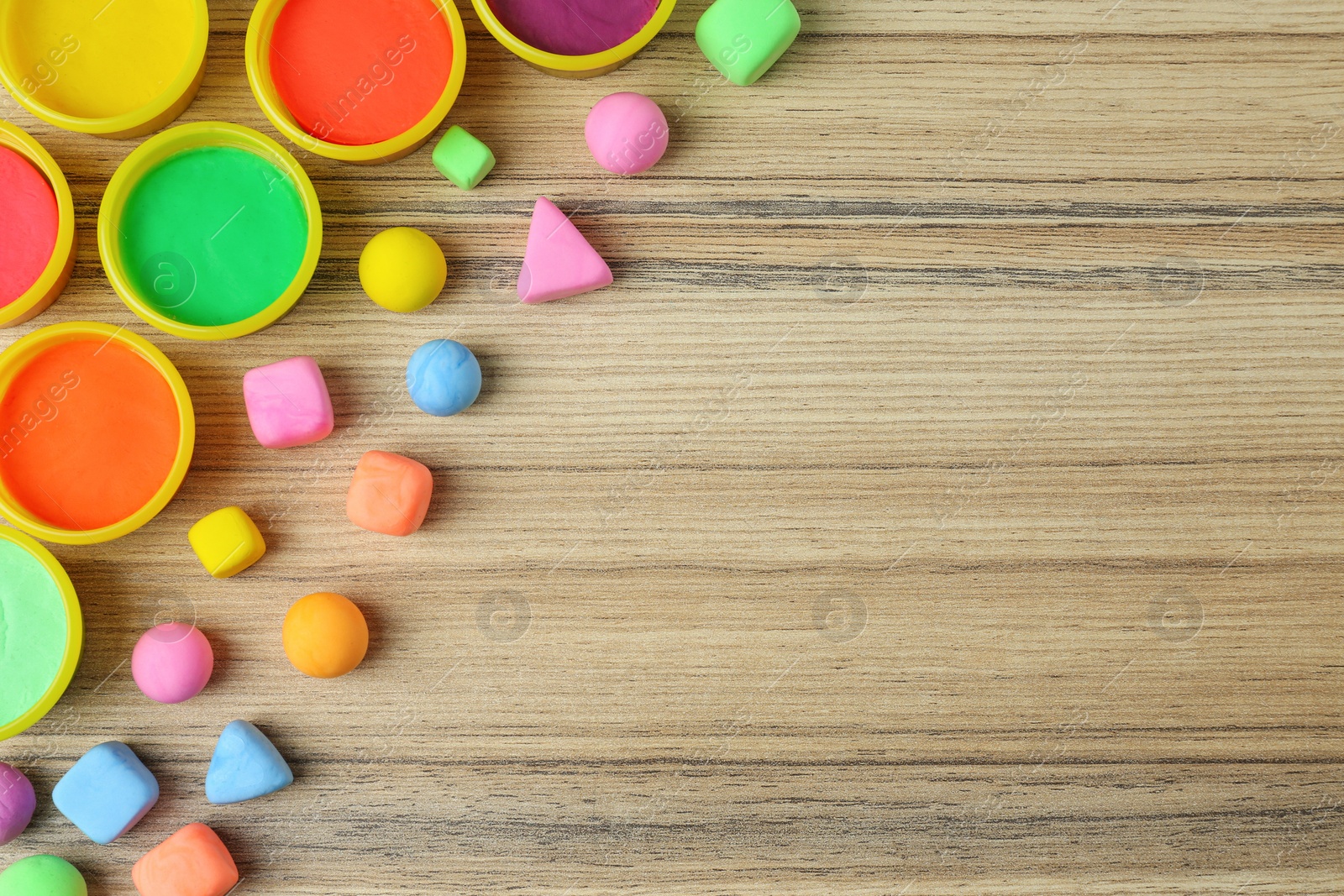 Photo of Different color play dough with plastic containers on wooden table, flat lay. Space for text