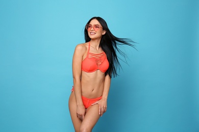 Beautiful young woman in stylish bikini with sunglasses on light blue background