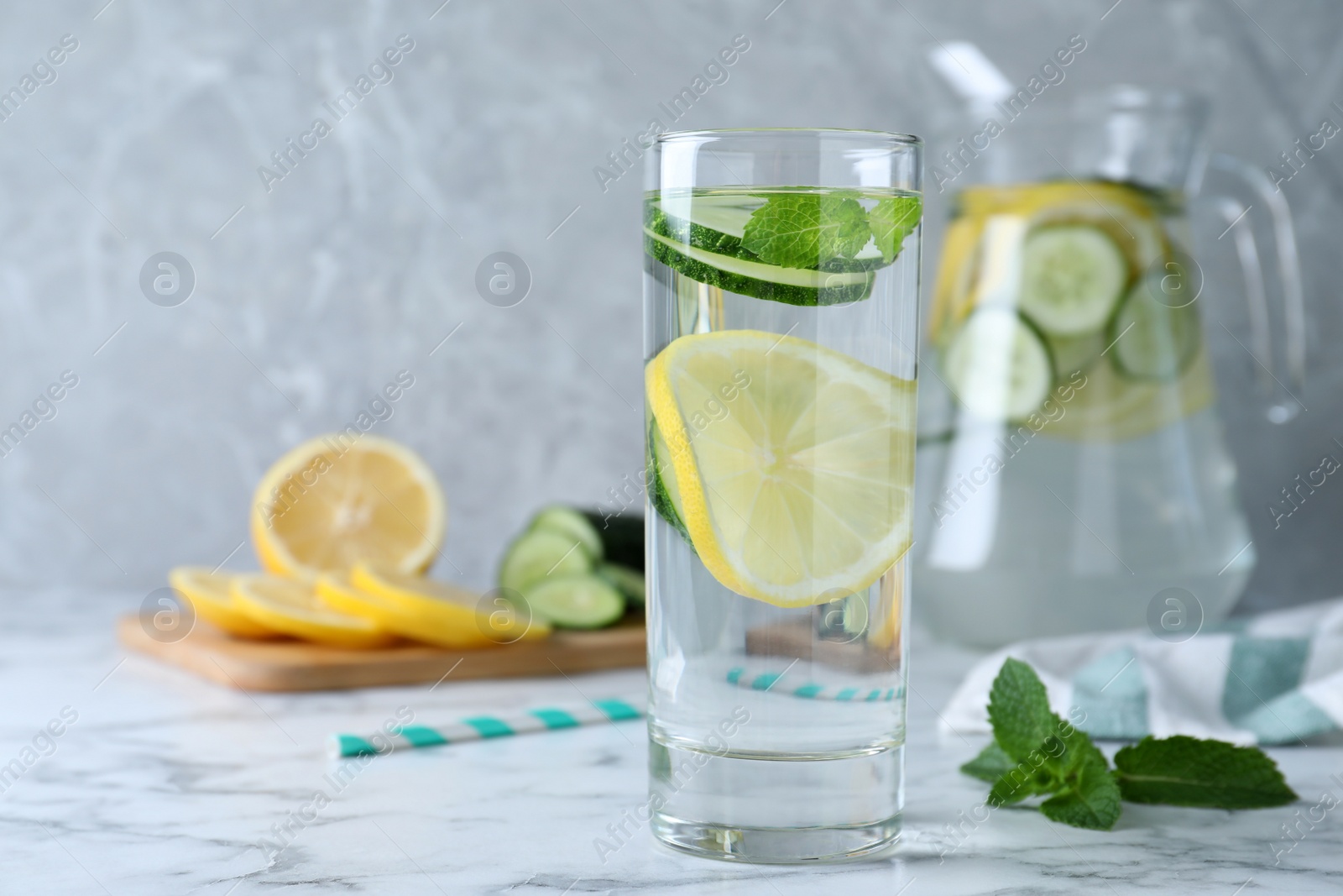 Photo of Refreshing water with cucumber, lemon and mint on white marble table. Space for text