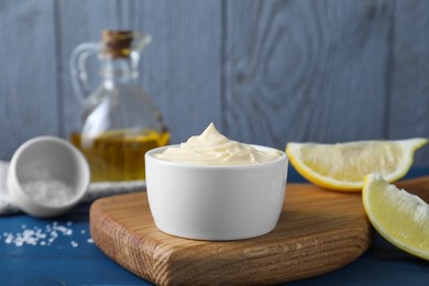 Photo of Tasty mayonnaise in bowl and lemon wedges on table, closeup