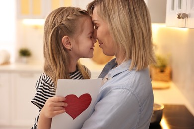 Little daughter congratulating her mom with greeting card in kitchen. Happy Mother's Day