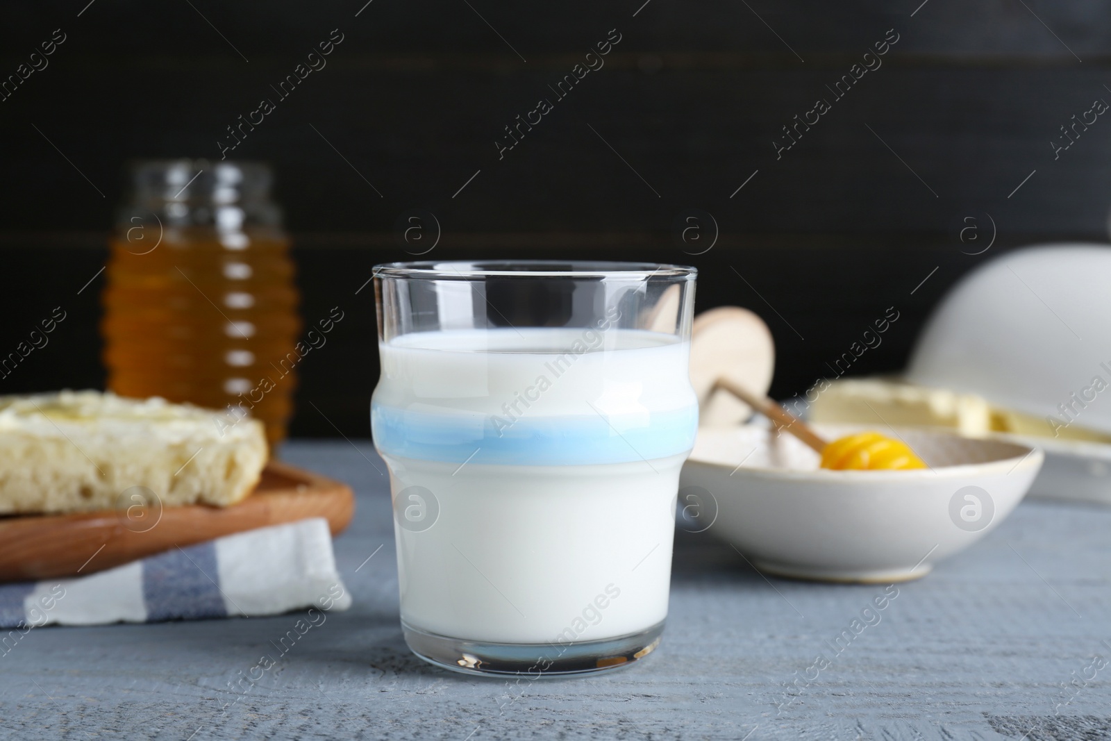 Photo of Glass with milk, honey, bread and butter on grey wooden table