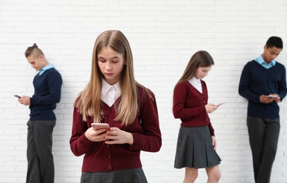 Photo of Teenagers using mobile phones at school. Concept of internet addiction and loneliness