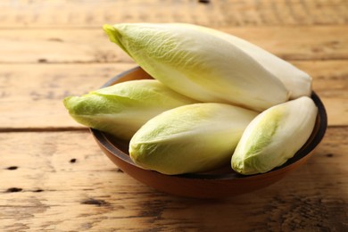 Photo of Fresh raw Belgian endives (chicory) in bowl on wooden table
