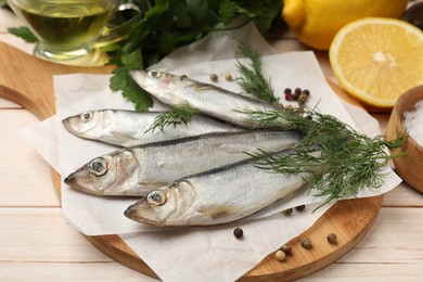 Photo of Fresh raw sprats, peppercorns and dill on light wooden table, closeup