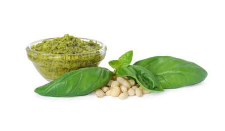 Photo of Delicious pesto sauce in bowl, pine nuts and basil leaves isolated on white