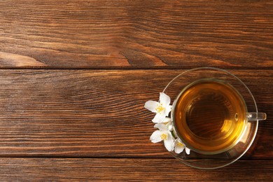 Photo of Glass cup of aromatic jasmine tea and fresh flowers on wooden table, top view. Space for text