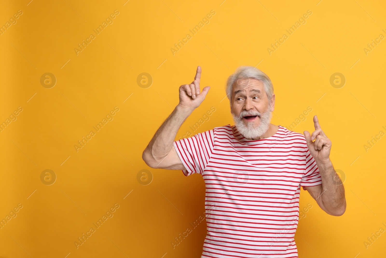 Photo of Senior man with mustache pointing at something on orange background, space for text