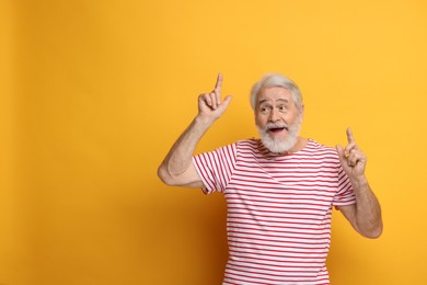 Senior man with mustache pointing at something on orange background, space for text